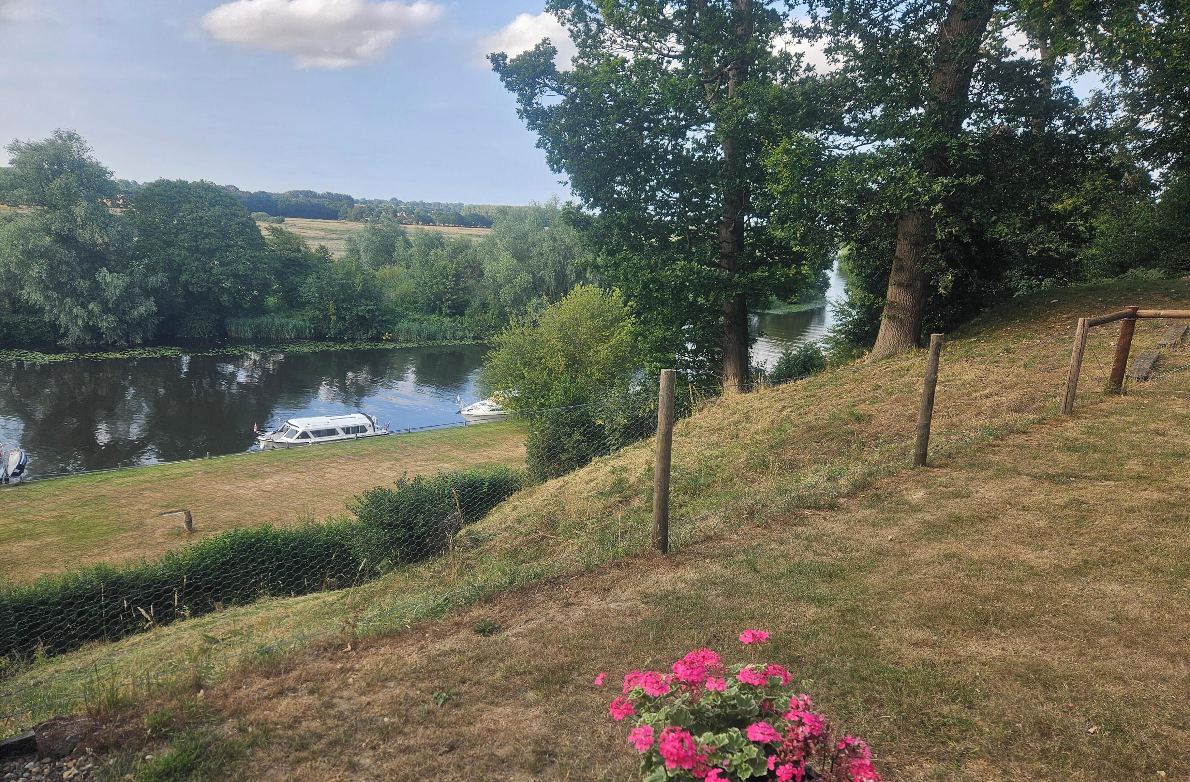 En flod med en båt förtöjd vid stranden, omgiven av träd och gräsbevuxna områden.