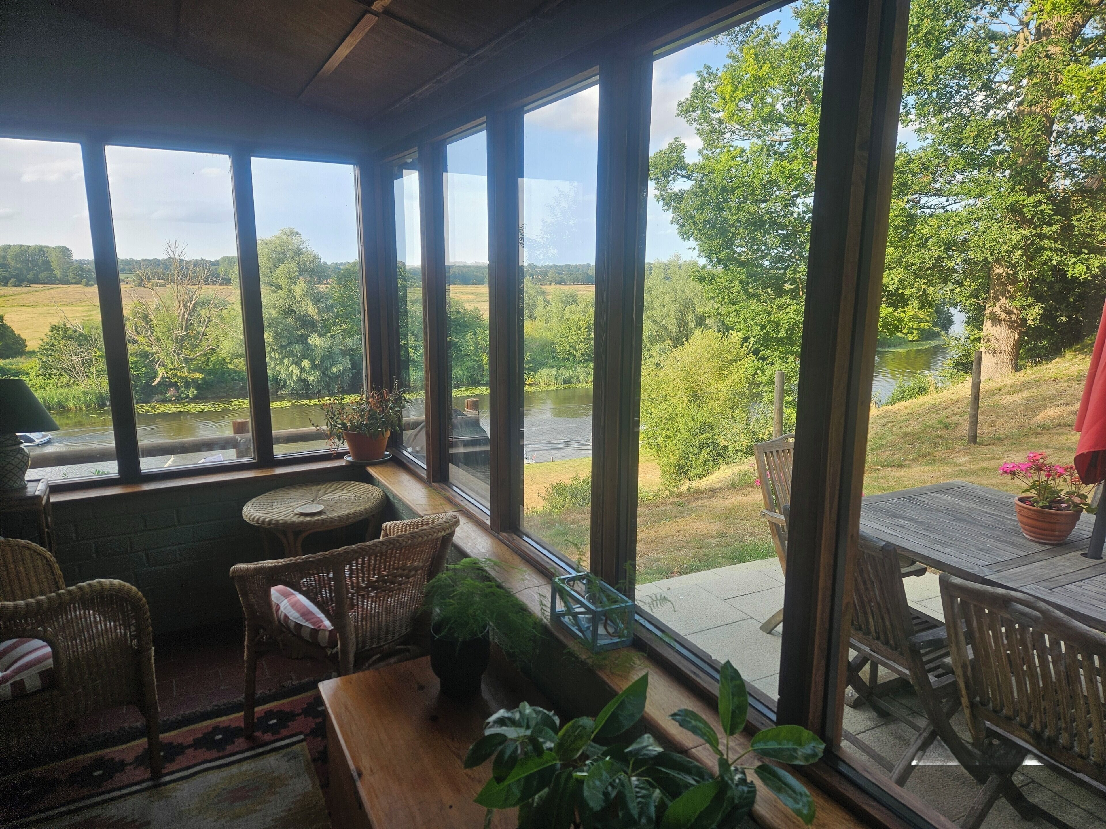 A room with large windows, wicker furniture, and a view of a river and greenery.