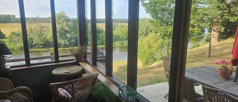 A room with large windows, wicker furniture, and a view of a river and greenery.