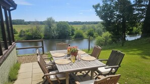 Een terras buiten, met een eettafel, uitkijkend op water en groen.