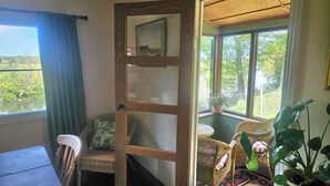 Een kamer met een houten deur die leidt naar een balkon, rieten meubels, een tafel en een potplant.