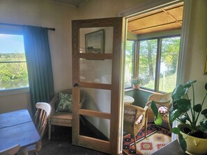 Ein Zimmer mit Holztür, die auf einen Balkon führt, Korbmöbel, einem Tisch und einer Topfpflanze.