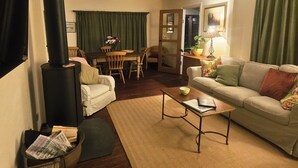 Een knusse woonkamer met een open haard, een bank, een bijzettafeltje en een eethoek met stoelen en een tafel.
