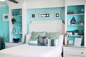 A bedroom with a bed, nightstands, a dresser, and shelves with decorative items. - Stylish Deluxe Gulf View studio, with jacuzzi tub (Bradenton Beach)