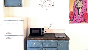 A kitchen area with a white refrigerator, a microwave on a wooden cabinet, and a clock on the wall.