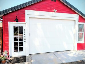 A red building with a white garage door, a white door with a window, and a mailbox on the right side.