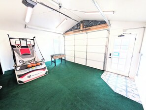 A room with a green carpet, a basketball hoop, and a foosball table.