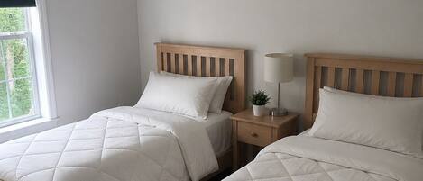 Une chambre avec deux lits simples, une table de chevet avec une lampe et une fenêtre avec des stores.