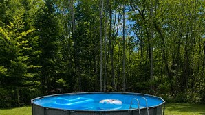 En rund pool som står ovan jord, med en stege på höger sida. Poolen är omgiven av en gräsyta och har träd i bakgrunden.