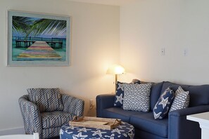 Ein Wohnzimmer mit einer Couch, einem gemusterten Sessel, einer Lampe und einem gerahmten Bild mit Strandmotiv.