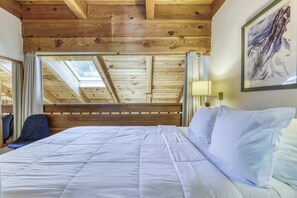 A bedroom with a wooden ceiling, a bed with white bedding, a chair, a window with curtains, and a framed picture on the wall. - Condo at Granlibakken Tahoe Resort - Ski-In - Ski-Out with Pool, Spa & Minutes from Lake Tahoe (Tahoe City)