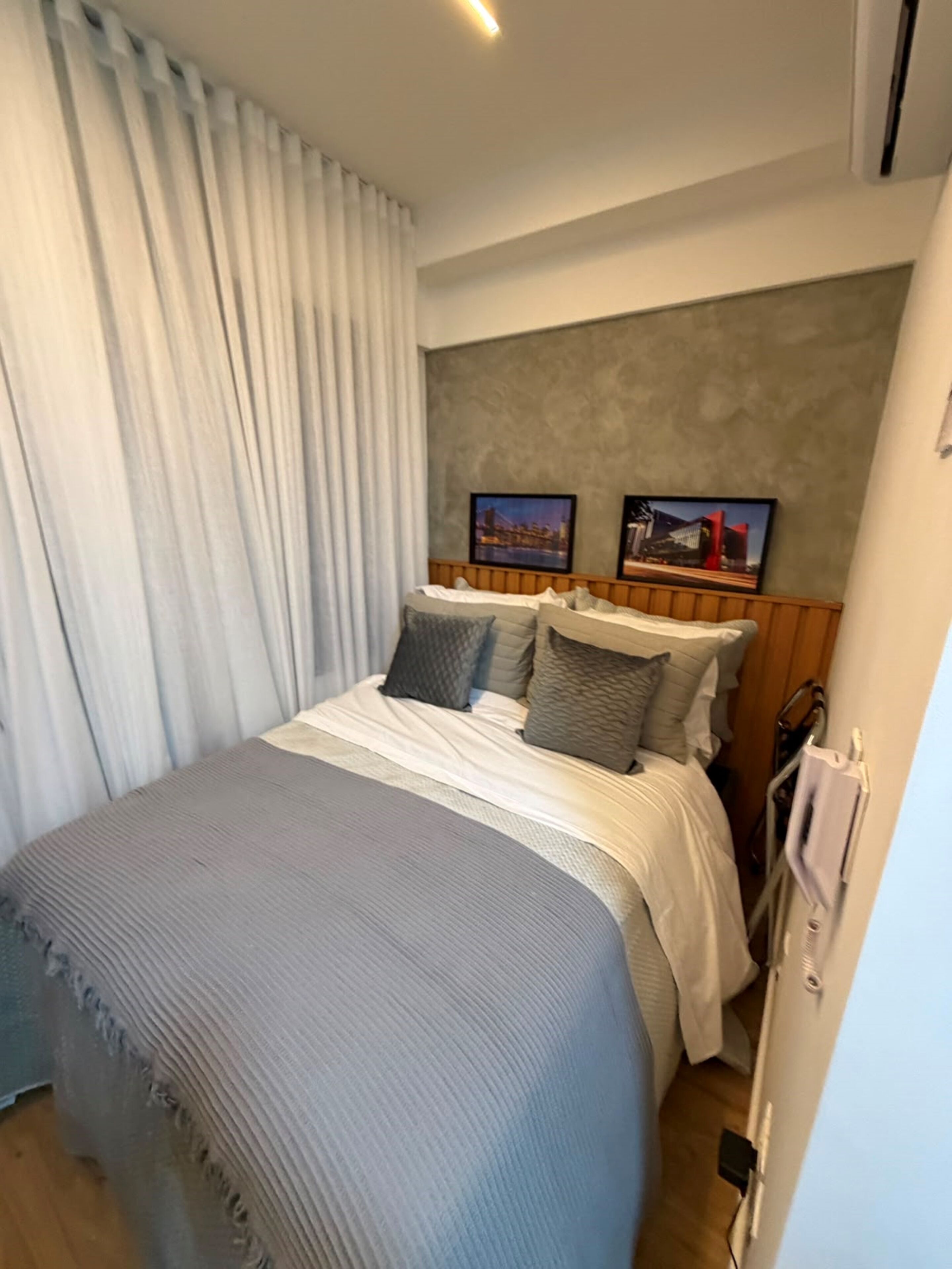 Ein Hotelzimmer mit Bett, Kopfteil, einem Fenster mit Vorhängen und einem Wandbild.