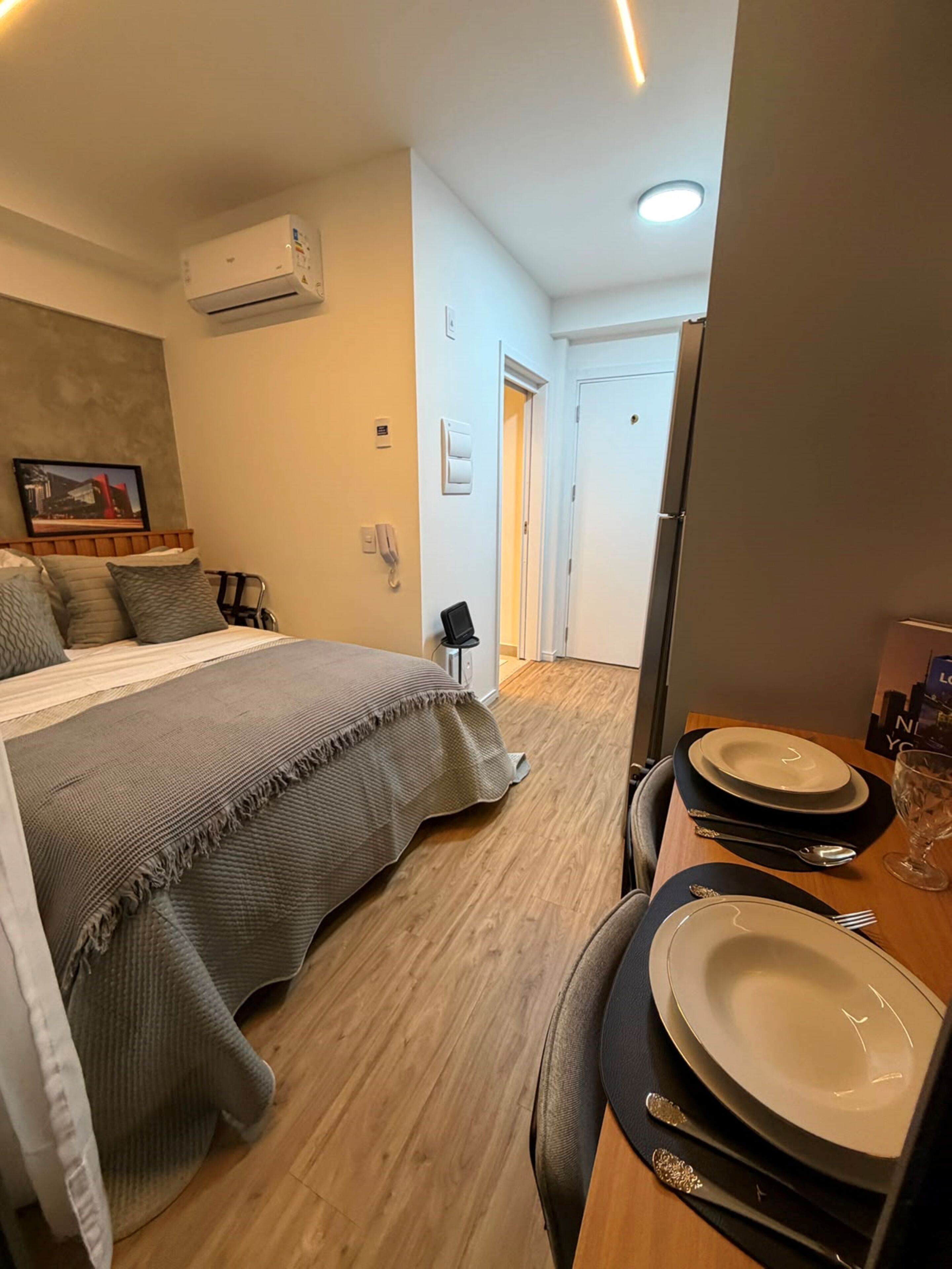 A hotel room with a bed, bedside table with a phone, a small table set for dining, and a door leading to another room.