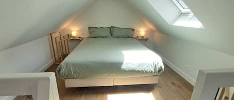 A bedroom with a sloped ceiling, a bed, bedside lamps, and a skylight.