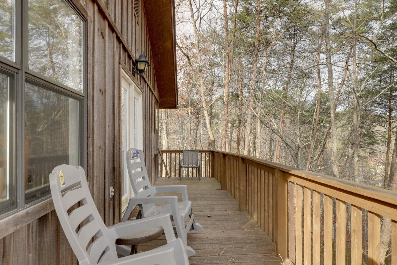 A wooden deck with chairs and a table, overlooking a forested area.