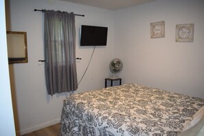 A bedroom with a bed, a TV mounted on the wall, a fan on a small table, and a curtain. - Heavenly Mountain View | Peaceful Cabin Escape (Sevierville)
