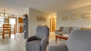 Een woonkamer met een bank, fauteuils, een salontafel, een eethoek met een houten tafel en stoelen, en een keuken met een koelkast en een spoelbak.