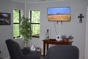 Ein Zimmer mit an der Wand montiertem Fernseher, einer Pflanze, einem kleinen Tisch mit einem Schild und zwei Stühlen.