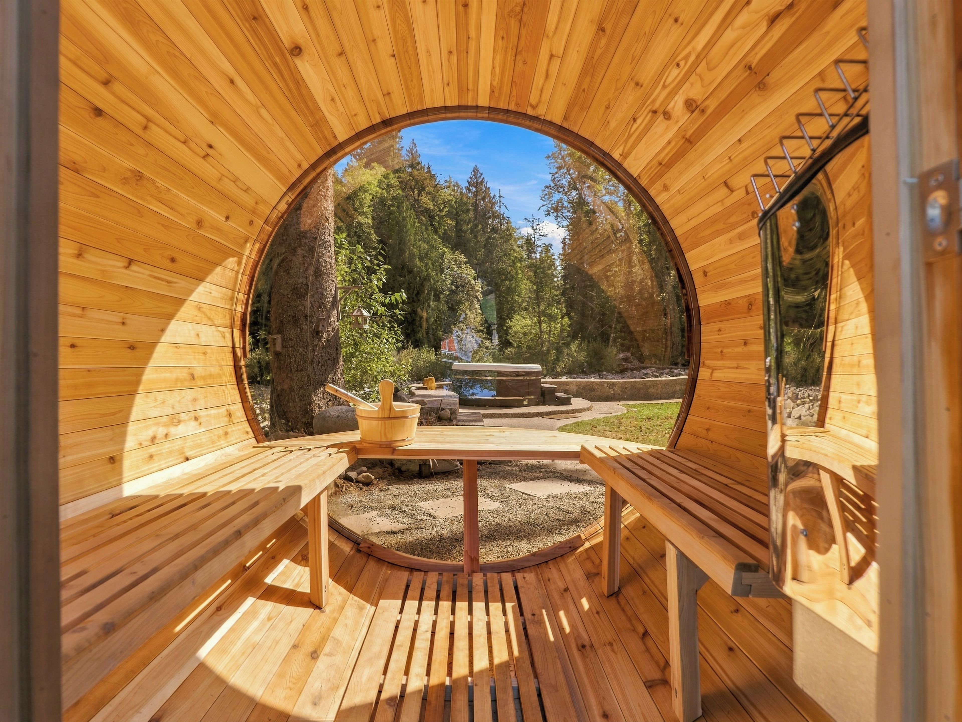 A wooden sauna with benches and a view of a forested area outside.