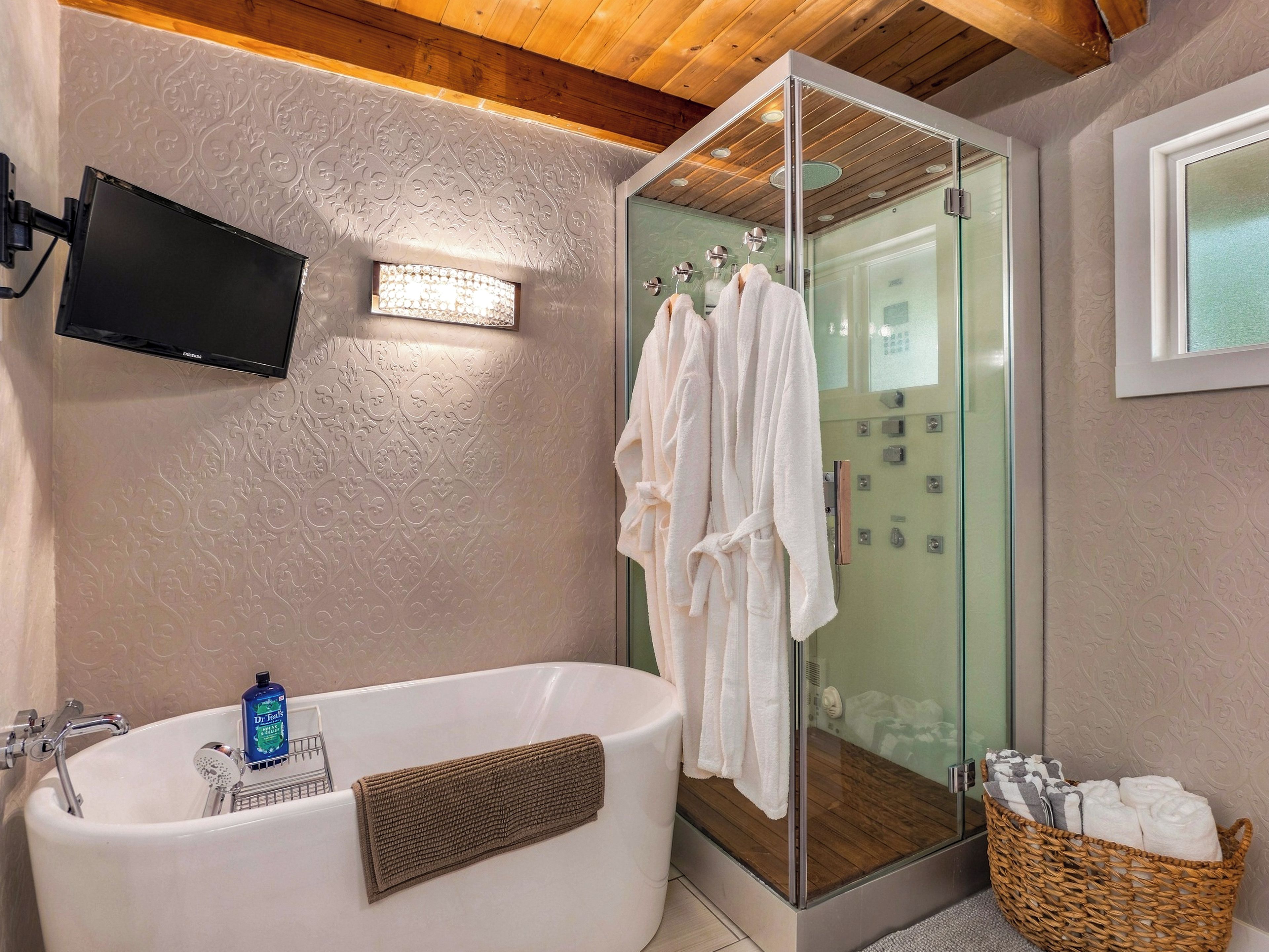 Ein modernes Badezimmer mit einer gläsernen Duschkabine, einer großzügigen Badewanne und einem an der Wand montierten Fernseher.