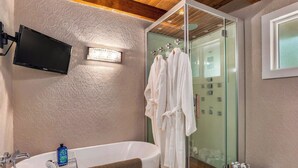 Une salle de bain moderne avec une douche à parois de verre, une grande baignoire et un téléviseur fixé au mur.