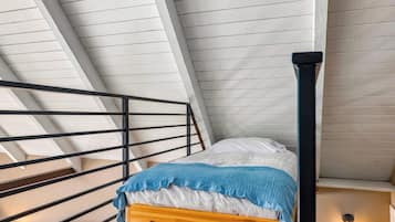 A bedroom with a sloped ceiling, a wooden bed, a black metal railing, and a wall-mounted light fixture.
