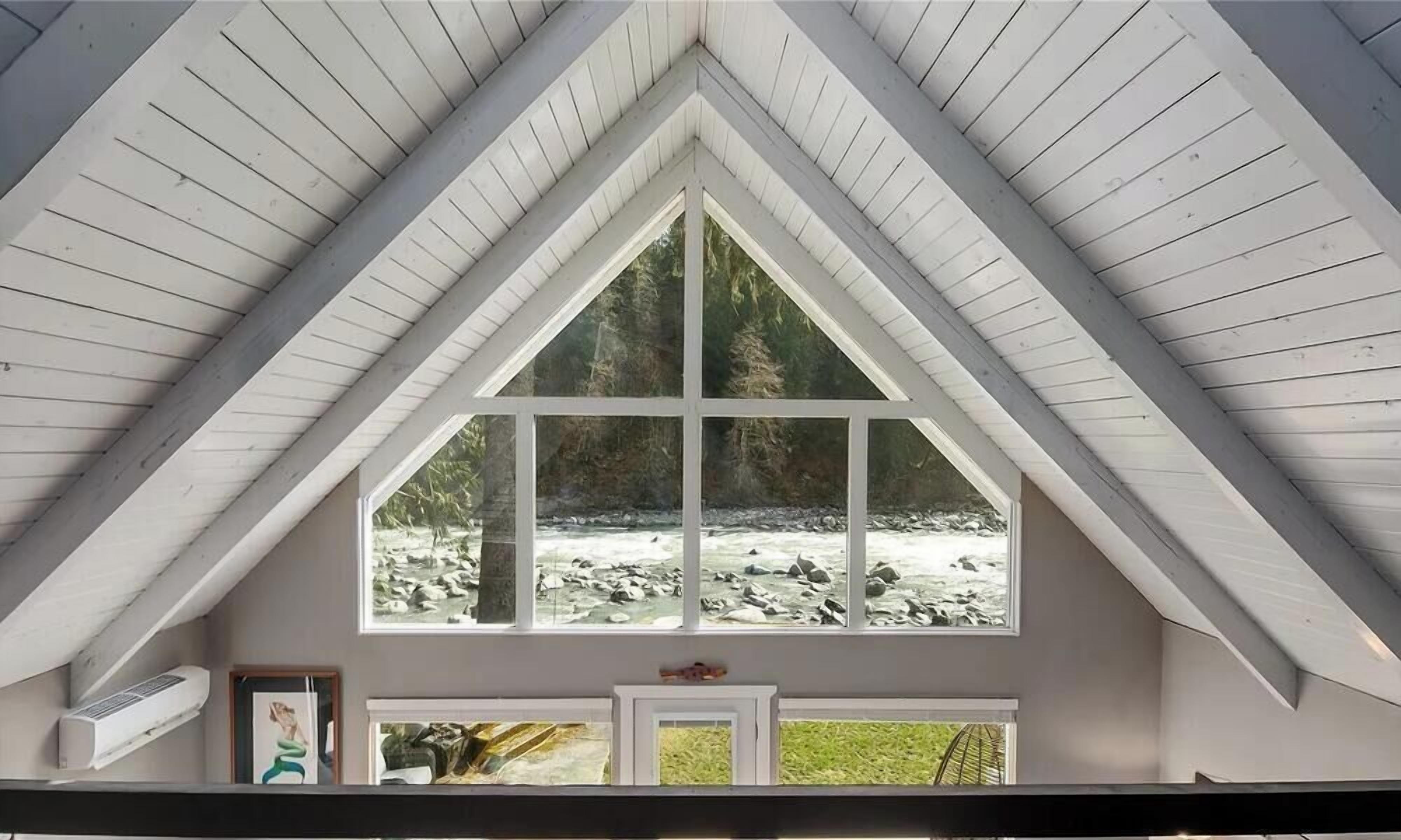 A room with a large window overlooking a rocky stream, a white ceiling, and a door with a small picture frame.