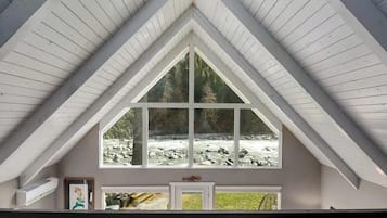 A room with a large window overlooking a rocky stream, a white ceiling, and a door with a small picture frame.