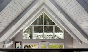 A room with a large window overlooking a rocky stream, a white ceiling, and a door with a small picture frame.
