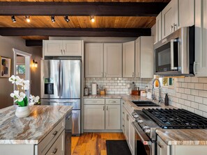A modern kitchen with stainless steel appliances, marble countertops, and wooden ceiling beams.