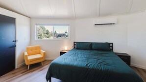A bedroom with a bed, a chair, a window, and an air conditioning unit. - Central Carousel (Bend)