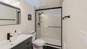 A modern bathroom with a glass-enclosed shower, a white toilet, and a vanity with a mirror and sink. - Central Carousel (Bend)
