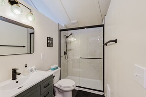 Ein modernes Badezimmer mit einer Duschkabine, einer weißen Toilette und einem Waschbecken mit Spiegel.