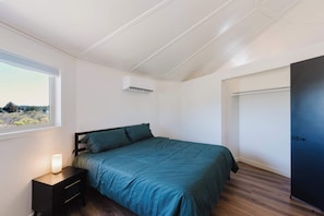 Ein Schlafzimmer mit Bett, Nachttisch, Lampe, Klimaanlage und Blick durch ein Fenster.