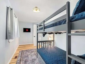 A bunk bed room with a television and a door leading to another room.