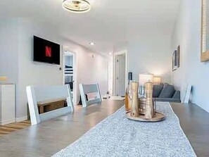 A modern living room with a dining table, a TV mounted on the wall, and a sofa.