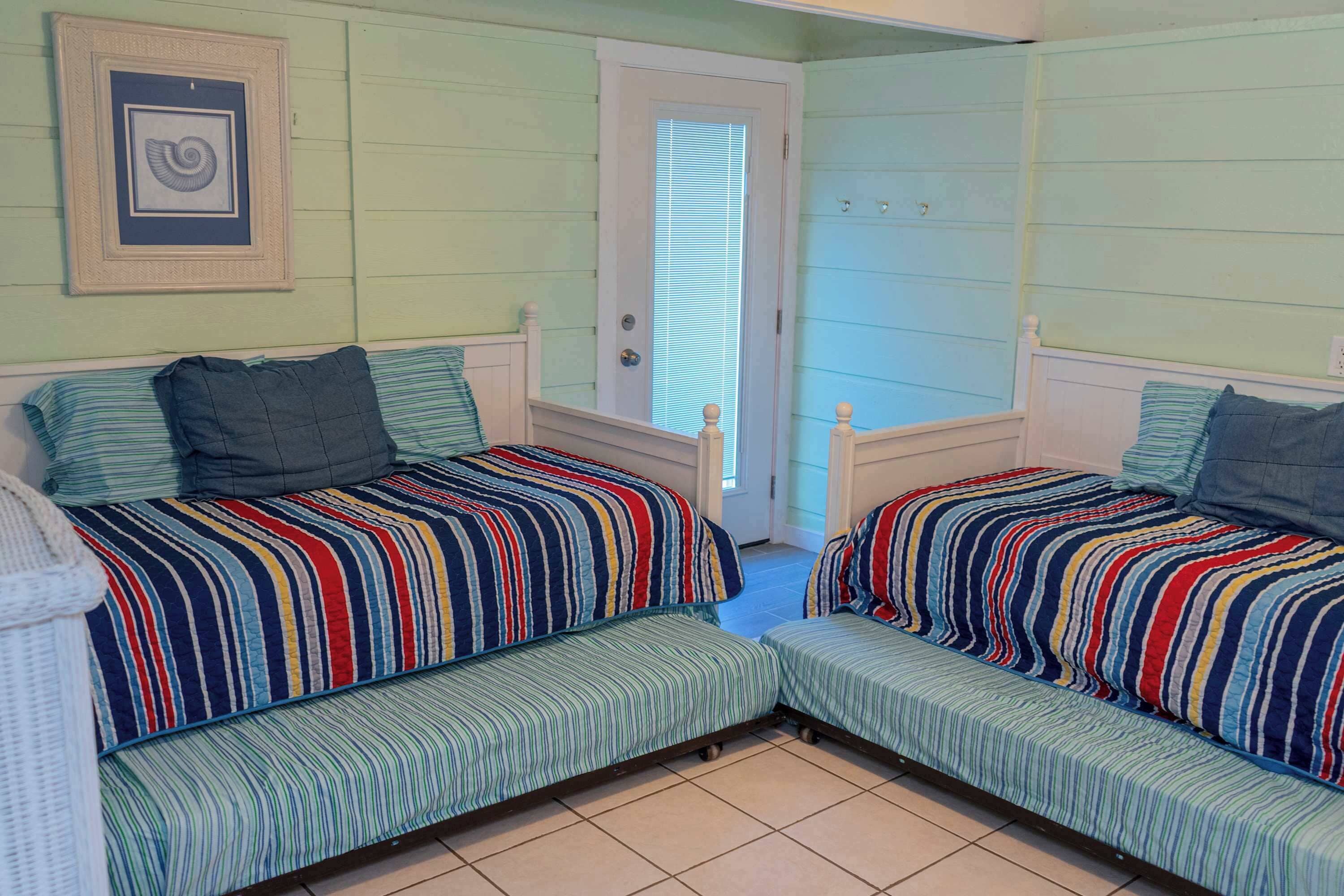A room with two beds, a door, and a framed picture on the wall.