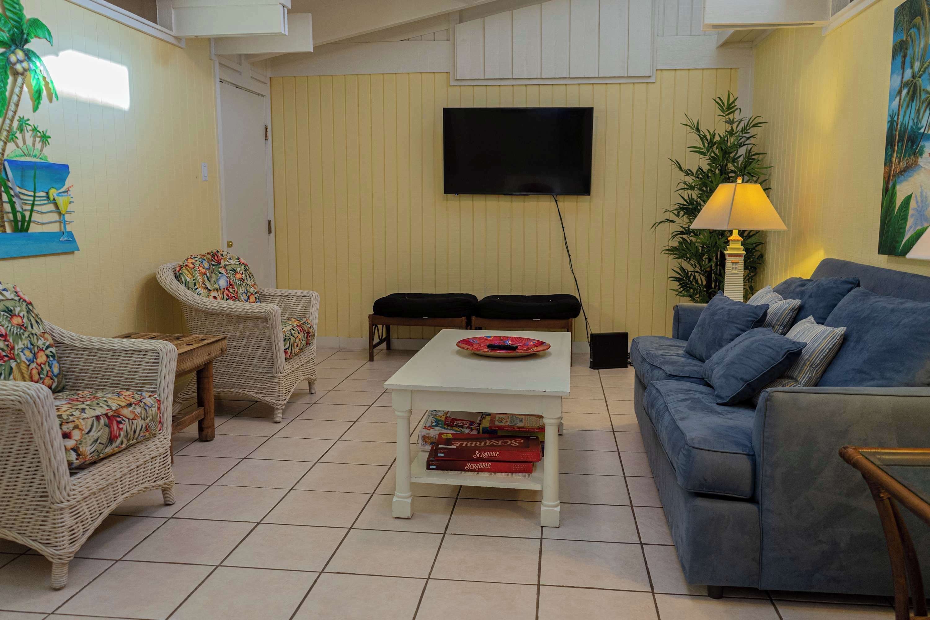 A living room with wicker furniture, a flat-screen TV, a lamp, and a painting on the wall.