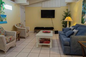 A living room with wicker furniture, a flat-screen TV, a lamp, and a painting on the wall. - Authentic Near Beach House - 5 Bedroom House (South Padre Island)