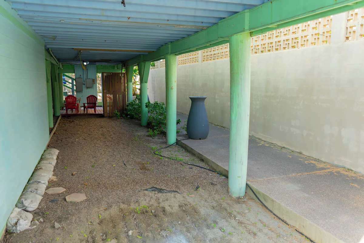 A covered corridor with a concrete floor, green pillars, and a large grey vase.