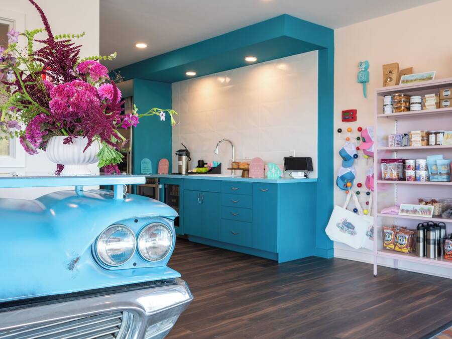 Una cocina con un coche azul, un jarrón blanco con flores y una estantería blanca con varios objetos.