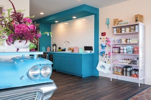 A kitchen with a blue car, a white vase with flowers, and a white shelf with various items.
