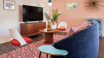Una sala de estar moderna con un televisor de pantalla plana grande, una mesa redonda de centro, un sofá azul y un tapete de diseño rojo y blanco.