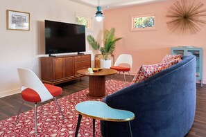 A modern living room with a large flat-screen TV, a round coffee table, a blue sofa, and a red and white patterned rug.