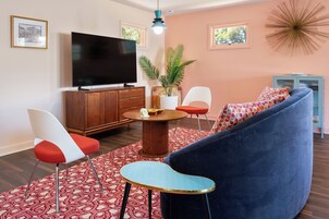 Una sala de estar moderna con un televisor de pantalla plana grande, una mesa redonda de centro, un sofá azul y un tapete de diseño rojo y blanco.