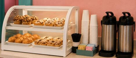 Vitrine de pastelaria com doces e uma estação de café com chávenas e termos.