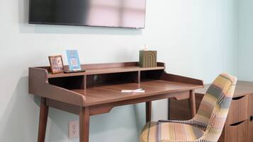 A room with a wooden desk, a chair, a television mounted on the wall, and a small cabinet.