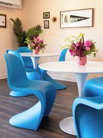 Un comedor moderno con sillas azules y mesas blancas, decorado con arreglos florales rosados.