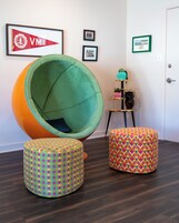 Una habitación con un sillón de cuero verde grande, dos otomanes coloridos y un cuadro con un emblema militar en la pared.