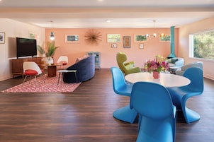 A modern living room with a flat-screen TV, a sofa, a dining table with chairs, and a large window with a view.